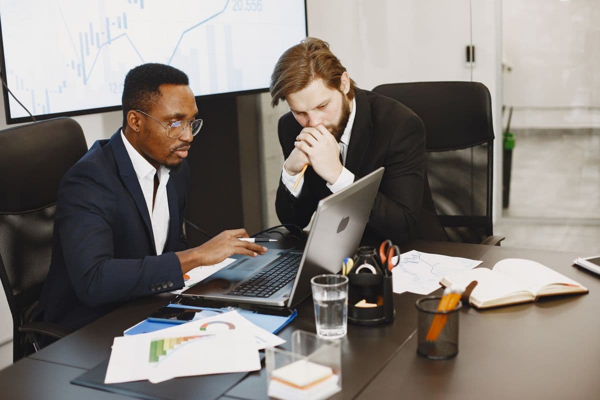 Two people in an office reviewing laptops and printed charts together