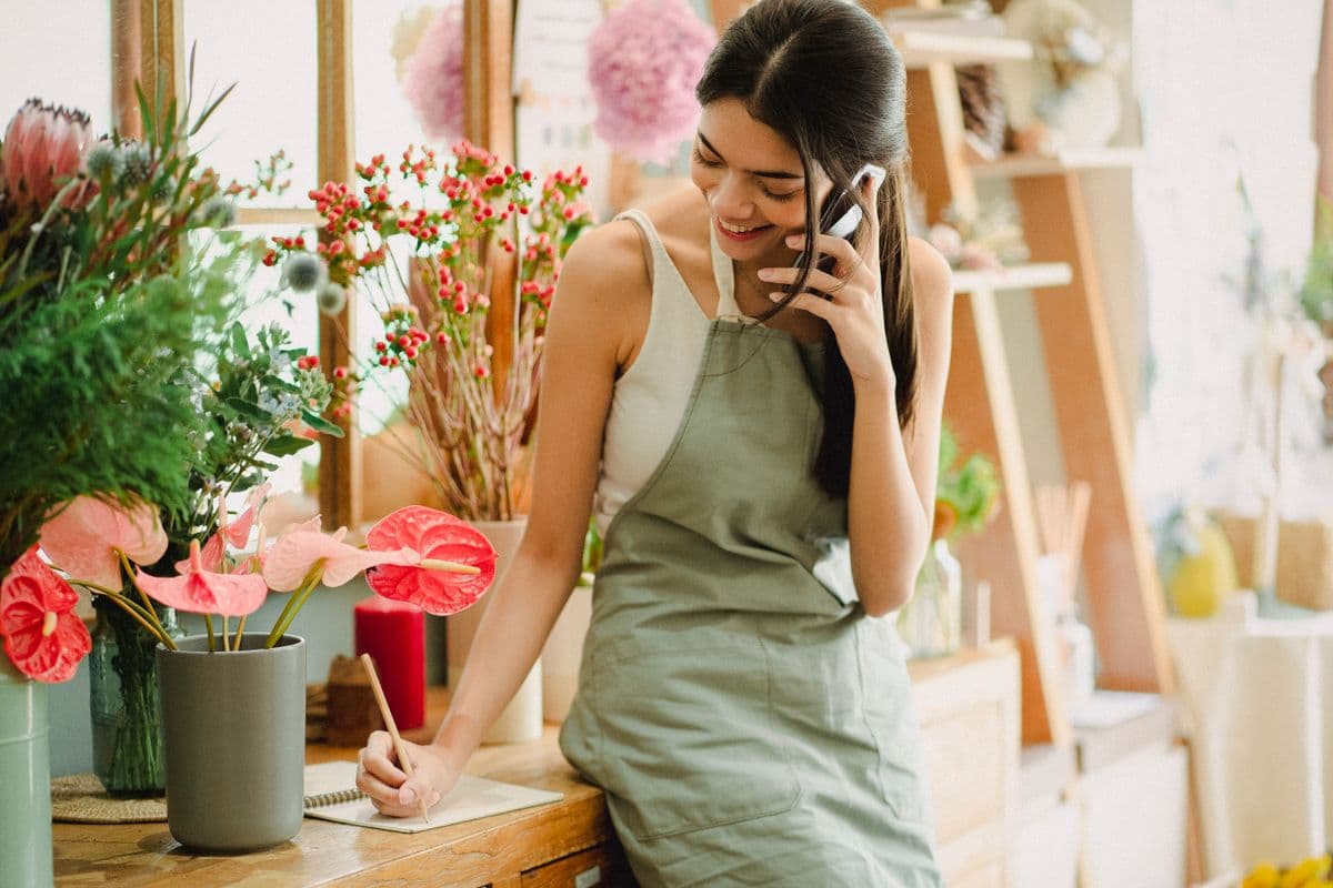 A Filipino small business owner taking a call while writing in a notebook at her flower shop